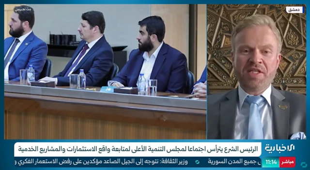 طلال محمود هلالی، سمت راست، در مصاحبه با شبکه دولتی الاخباریه السوریه
