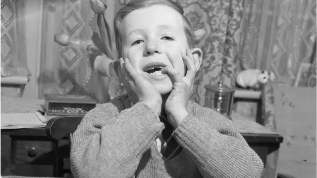 niño rubio con codos en la mesa y rostro apoyado en sus mejillas