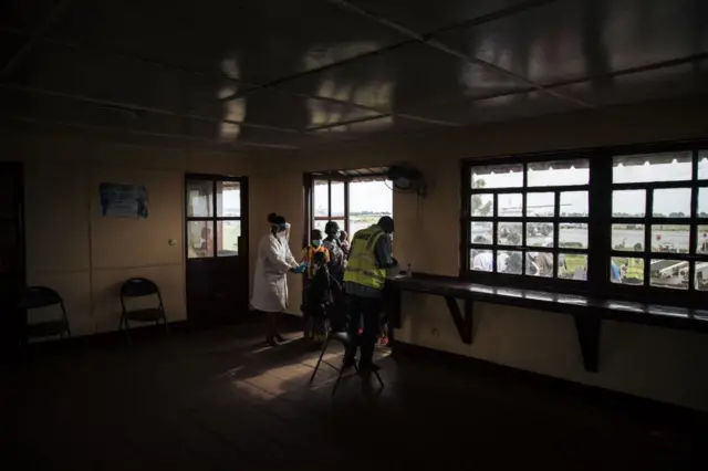 Central African medical authorities at the Bangui airport hold refugees arriving from the repatriation flight from northern Democratic Republic of Congo for screening and vaccination on November 15, 2021. - Between November 15 and 20, 453 amongst Inke's 18,444 refugees are being flown back to Bangui by the United Nations High Commissioner for Refugees (UNHCR)