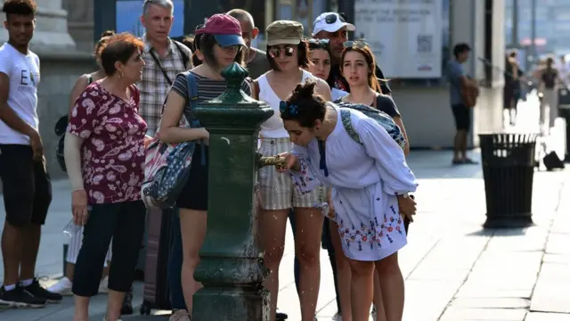 Люди стоять в черзі, щоб пити воду з фонтану з питною водою біля собору Дуомо в Мілані