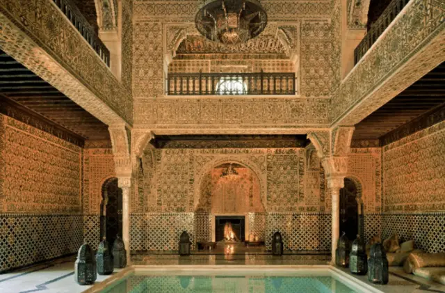 Kryty basen z niezwykle dekoracyjnym kominkiem na jednym końcu, żyrandolem i dużymi marokańskimi lampami po obu stronach basenu