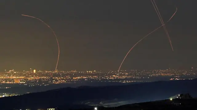 夜空に光の曲線が数本走っている。地上には建物の明かりが広がっている