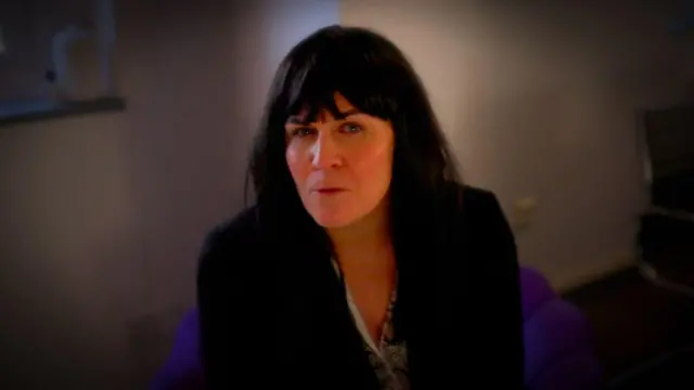 Una mujer con cabello oscuro sentada dentro de una habitación oscura.