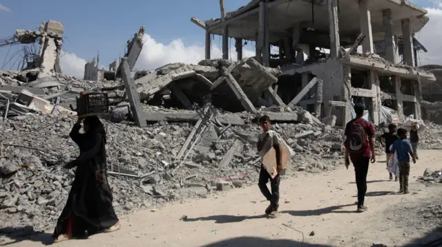 Палестинцы на фоне разрушенного здания в Хан-Юнисе