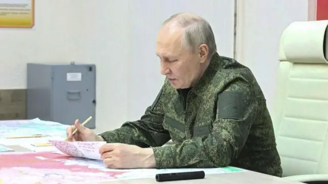 Rusya Devlet Başkanı Vladimir Putin, askeri üniformasıyla oturuyor ve haritaları inceliyor. Tek başına görünüyor.