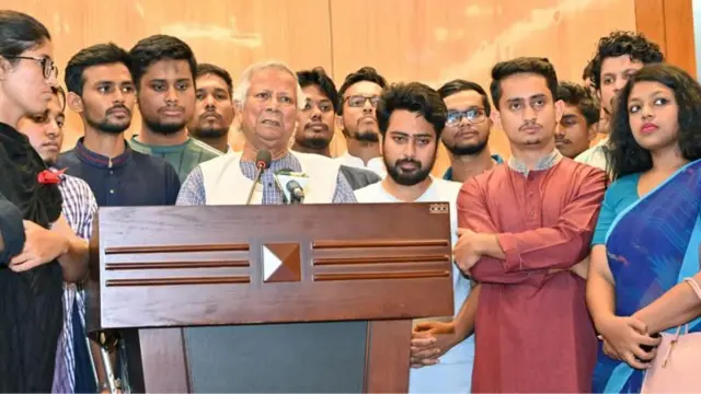 ২০২৪ সালের অগাস্টে ফ্রান্স থেকে ঢাকায় ফিরে সেই সময়ের বৈষম্যবিরোধী ছাত্র নেতাদের সঙ্গে সংবাদ সম্মেলনে মুহাম্মদ ইউনূস, তার পেছনেই জার্সি গায়ে হাসনাত