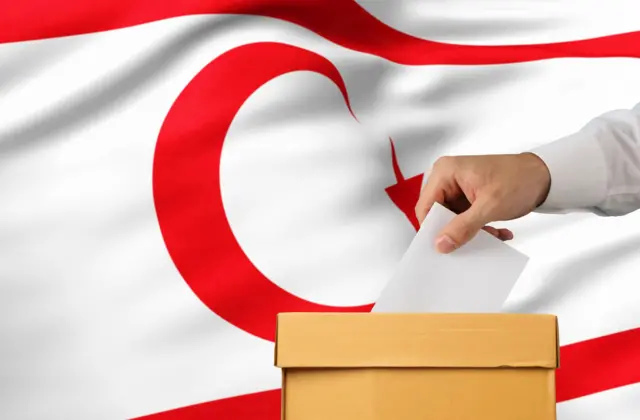 یک دست که در حال انداختن رای در صندوق انتخابات است، پسزمینه پرچم قبرس شمالی است