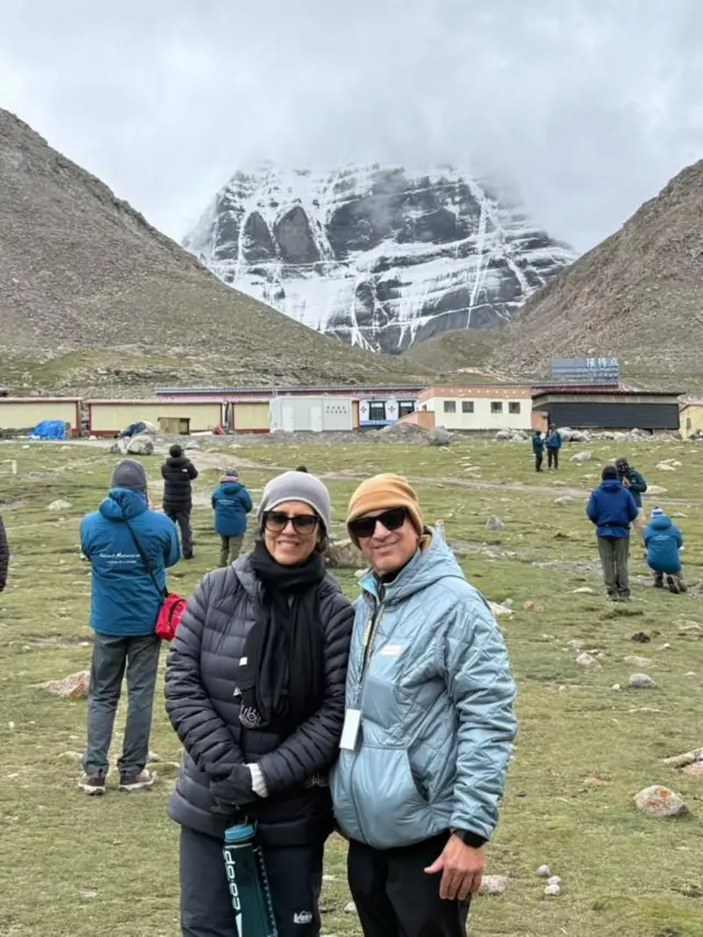 Deepak y Madhu Ahuja cerca del Monte Kailash. Ambos están fuertemente abrigados frente a una montaña nevada. 