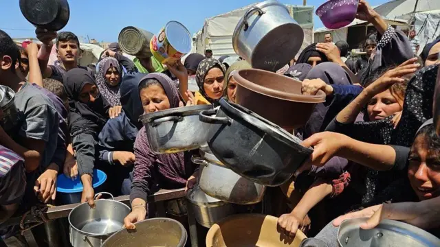 Palestinians wait in queues to receive food from the charity organization that distributes hot meals, as the food crisis is deepening due to the closed border crossings amid Israeli attacks at the al-Mawasi area in Khan Yunis, Gaza on May 21, 2025.