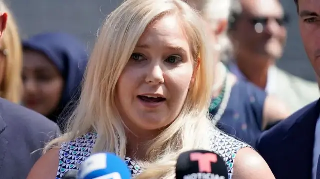 ویرجینیا جوفری در فضای باز، در حالی که تعدادی از مردم او را احاطه کرده بودند، پشت میکروفون سخنرانی می‌کرد