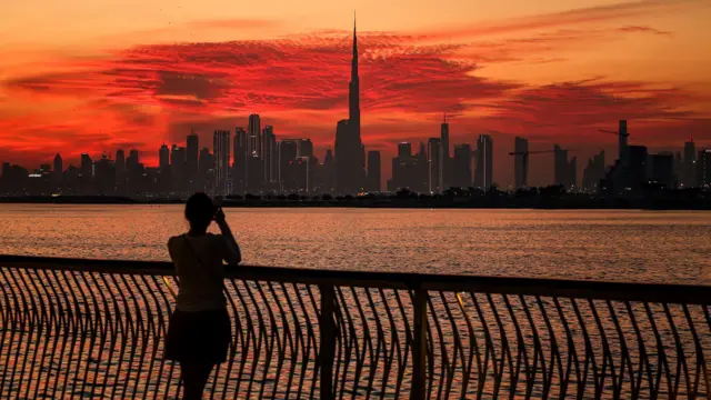 امرأة تلتقط صورة لأفق دبي مع برج خليفة، أطول مبنى في العالم، كما يُرى من خور دبي في 5 فبراير/شباط 2025.