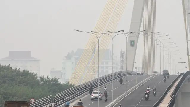 Sejumlah pengendara kendaraan bermotor melintas di atas jembatan Siak IV yang diselimuti kabut asap dampak kebakaran hutan dan lahan, di Pekanbaru, Riau, Selasa (06/08/2019).