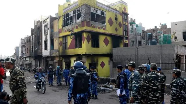 एक जले हुए मकान के बाहर खड़े सुरक्षाकर्मी