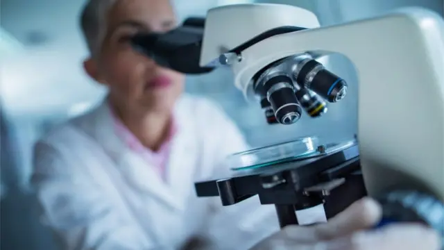 Жінка-науковець дивиться в мікроскоп