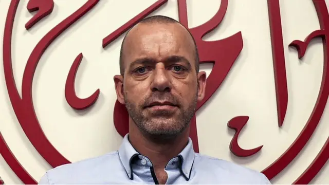 صلاح حموري، المحامي الفلسطيني الذي يحمل الجنسيتين الفلسطينية والفرنسية، يقف أمام شعار لمؤسسة الحق لحقوق الإنسان في رام الله بالضفة الغربية في صورة تعود إلى نوفمبر/ تشرين الثاني 2021