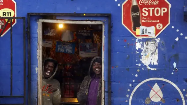 Men smile as they stand inside a shop hiding from rainfall, in Delft township on the outskirts of Cape Town, South Africa - Tuesday 26 July 2016