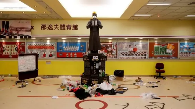 A statue, decorated with a yellow helmet and mask by anti-government protesters, is surrounded by garbage inside the student union building at the besieged Hong Kong Polytechnic University (PolyU) in Hong Kong