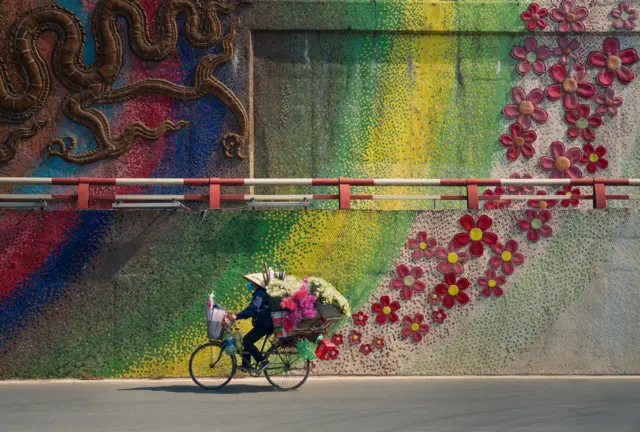 Person on a bike cycling past a colourful wall decorated with flowers