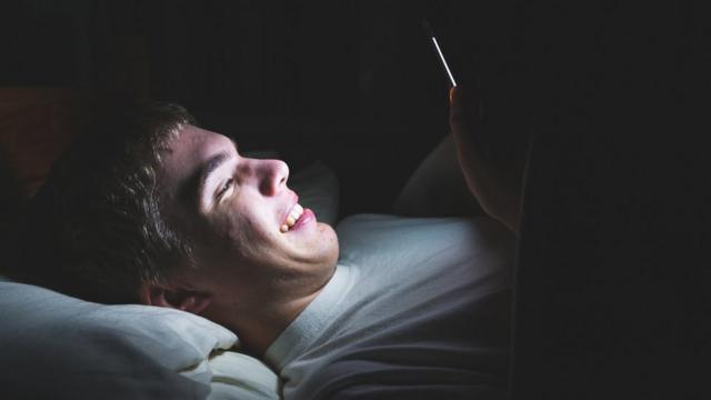 Teenage boy looking at his phone in the dark in bed