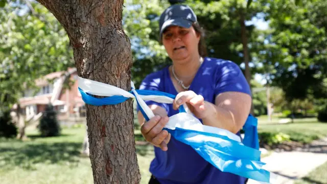Mujer atando lazos blancos y azules en un árbol