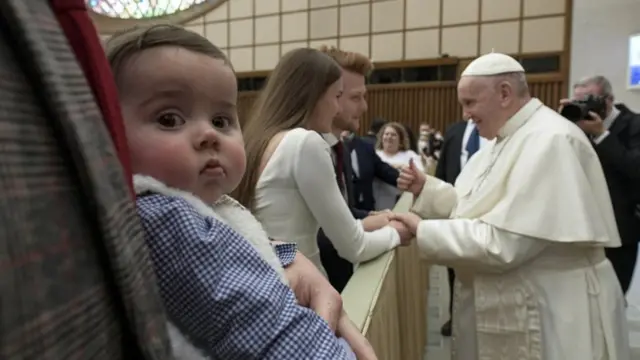 Bebê olha para a câmera, com papa conversando com casalroleta de nomes personalizadasegundo plano