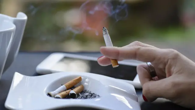 Mão feminina segurando um cigarro aceso