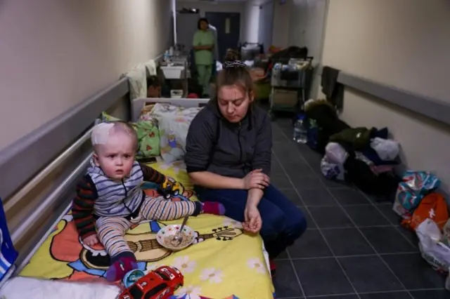 A woman sits next to a child patient whose treatments is underway, in the hallways of basement floors of Okhmadet Children"s Hospital, as Russia"s invasion of Ukraine continues, in Kyiv, Ukraine February 28, 2022