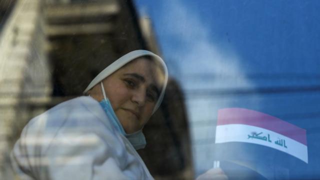 بغداد – راهبة عراقية ترفع علمي العراق والفاتيكان وهي تتوجه على متن حافلة إلى مطار بغداد للمشاركة في استقبال البابا