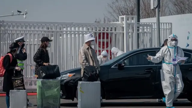 A worker (front R) wearing a protective suit as a preventive measure against the COVID-19 coronavirus stands next to passengers (L) at the New China International Exhibition Centre, near Beijing Capital Airport in Beijing on March 16, 2020.