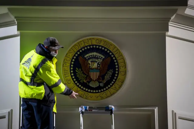 An Architect of the Capitol worker hangs up a Presidential seal