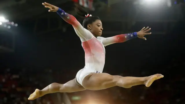 Simone Biles en un salto con las piernas abiertas a los lados.