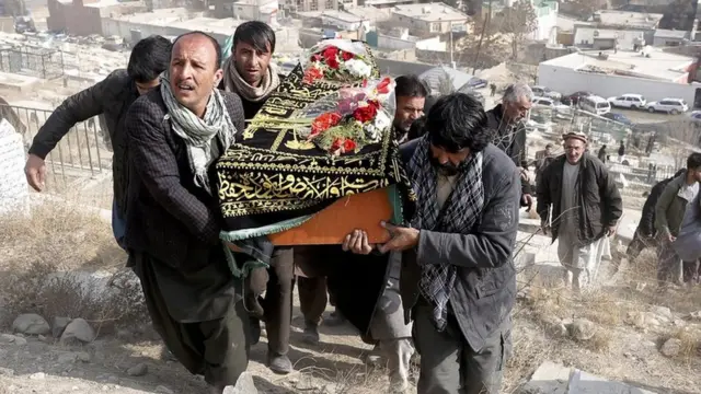 a group of men carrying a coffin up a dusty hill, with city buildings in the distance