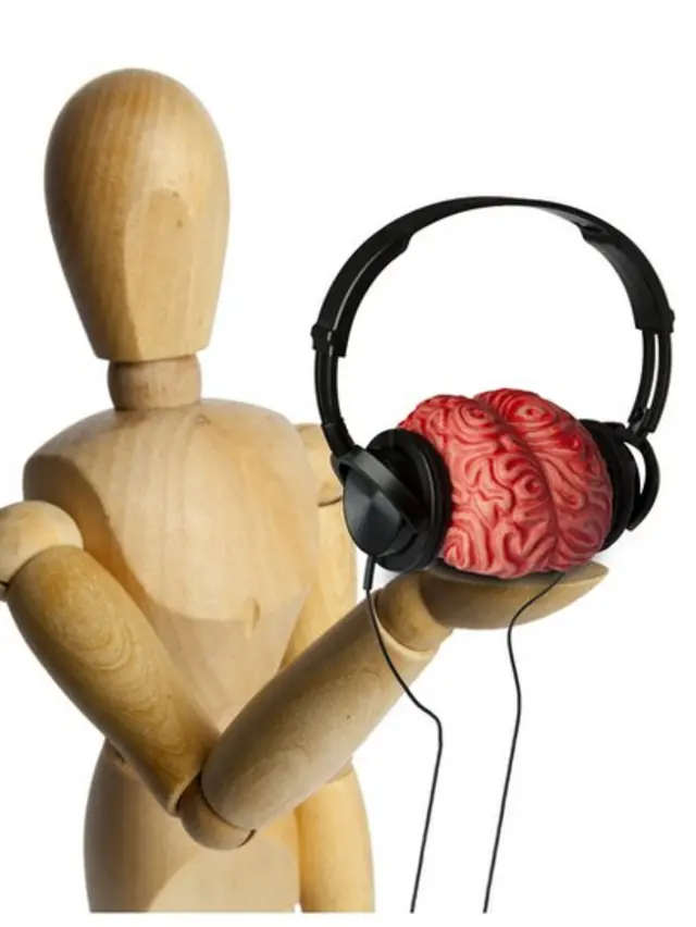 Muñeco de madera sosteniendo en una mano un cerebro con audífonos.