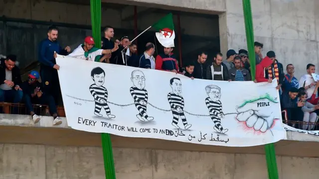 Des manifestants tiennent une banderole sur laquelle sont caricaturés des proches de Bouteflika.