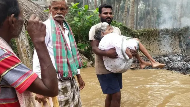 వరదలో చిక్కుకున్న వృద్ధురాలిని తరలిస్తున్న స్థానికులు