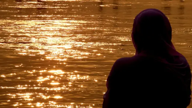 नदीकाठी सूर्यास्त पाहणारी एक स्त्री