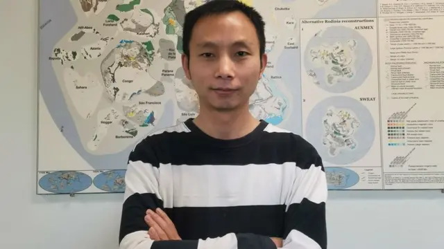 Chuan Huang de braços cruzados em frente a mapa em laboratório