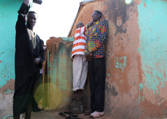 Um vizinho subiu em um banquinho para marcar a parede ao medir Awuche.