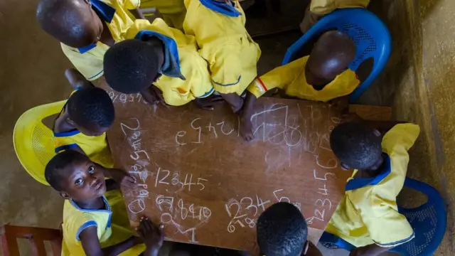 School children dey write ontop table.
