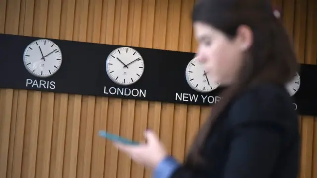 Годинники, що показують різні часові пояси, і дівчина з телефоном