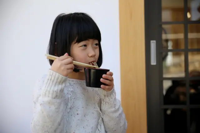 Cute Japanese girl, slurping noodles from a black bowl