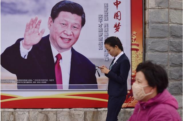 人们走过北京一条道路旁的“中国梦，人民的梦”海报，上面有中国国家主席习近平挥手的照片。
