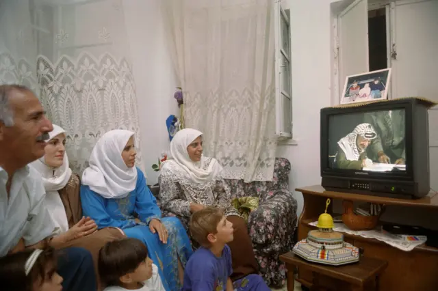 عائلة فلسطينية في القدس الشرقية المحتلة تشاهد ياسر عرفات وهو يوقع اتفاق أوسلو الثاني، في 28 سبتمبر/أيلول 1995