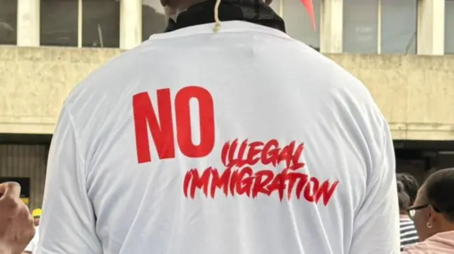 One protester wear shirt wey dem caption "No Illegal Migration".