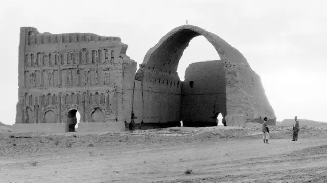 Una foto en blanco y negro de las ruinas de un monumento, con un gran arco ahuecado en un lado.