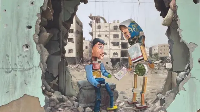 Une peinture murale représentant des marionnettes construites par Mahdy Krira à partir de boîtes de conserve entre un mur bombardé à Gaza.