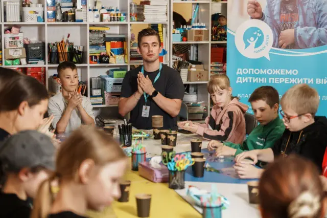 Дети за столом занимаются творчеством, в центре специалист фонда