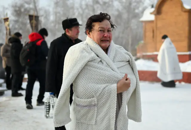 старија жена умотана у баде мантил после уласка у ледену воду током богојављања у русији