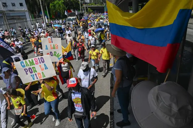 Marcha em rua na Colômbia com pessoas usando bandeiras 