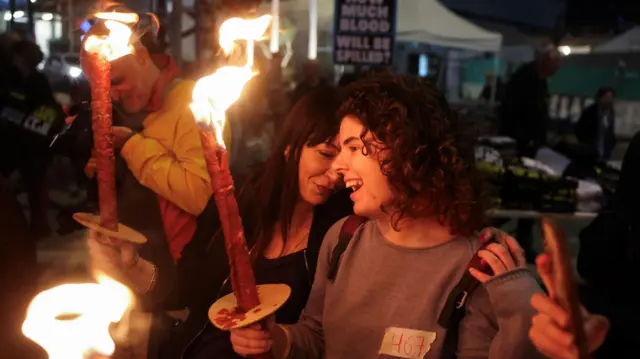 Duas mulheres sorrindo e segurando tochas durante protesto à noite 